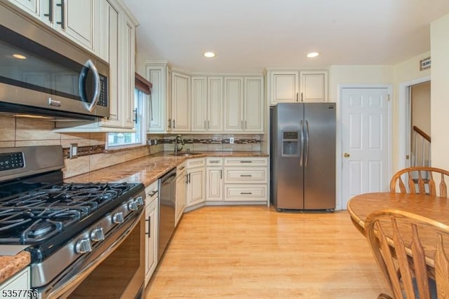kitchen featuring appliances with stainless steel finishes, a sink, light wood-style flooring, light stone countertops, and tasteful backsplash