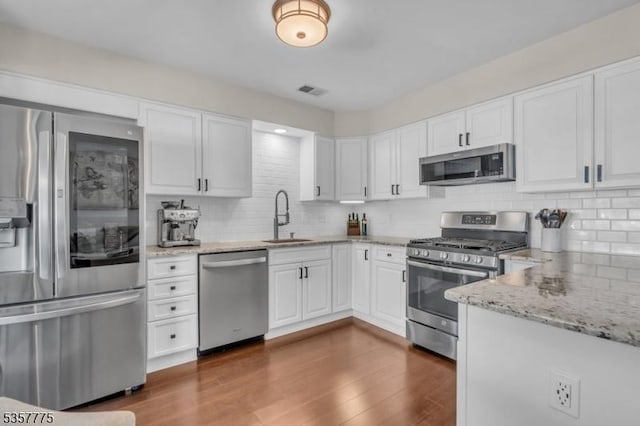 kitchen with appliances with stainless steel finishes, a sink, backsplash, and white cabinetry