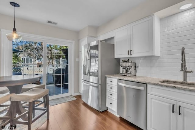 kitchen with appliances with stainless steel finishes, white cabinetry, a sink, and light stone countertops