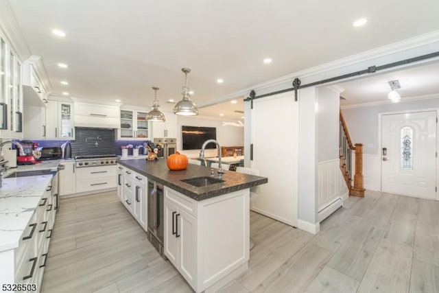 kitchen with a sink, a barn door, appliances with stainless steel finishes, an island with sink, and crown molding