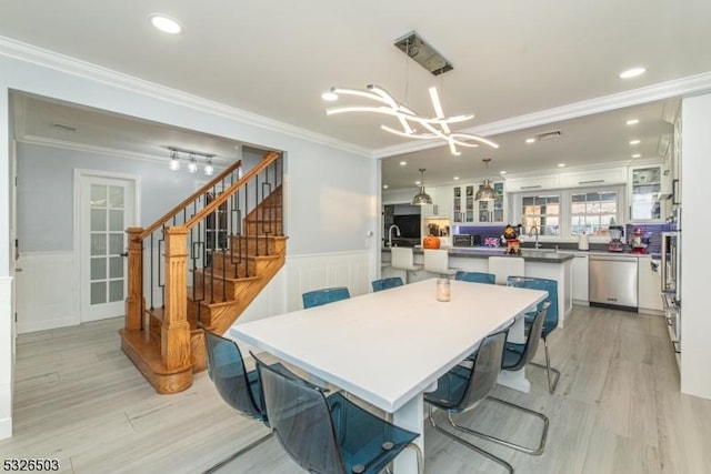 dining space with a chandelier, wainscoting, light wood finished floors, crown molding, and stairs