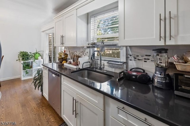 kitchen featuring dishwasher, a sink, decorative backsplash, dark wood-type flooring, and white cabinetry