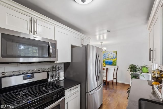 kitchen with appliances with stainless steel finishes, white cabinets, light wood-style floors, dark countertops, and tasteful backsplash