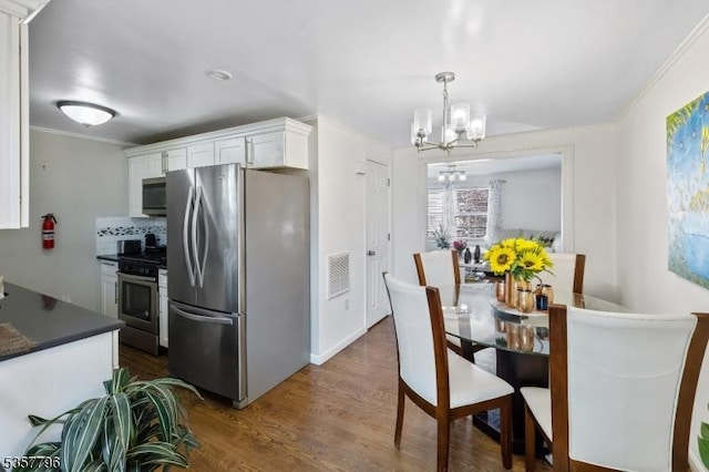 kitchen featuring stainless steel appliances, dark countertops, a chandelier, white cabinets, and dark wood-style flooring