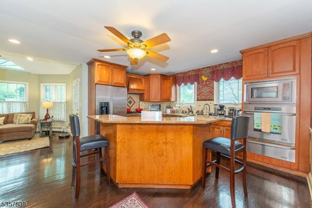 kitchen featuring appliances with stainless steel finishes, a warming drawer, dark wood-type flooring, a kitchen bar, and recessed lighting