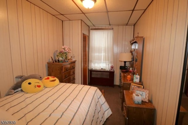 carpeted bedroom with a drop ceiling and wood walls