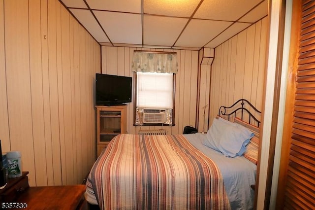 bedroom with a paneled ceiling, cooling unit, and wood walls