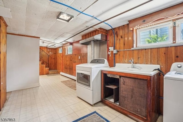 clothes washing area featuring washer / clothes dryer, wooden walls, light floors, and a sink