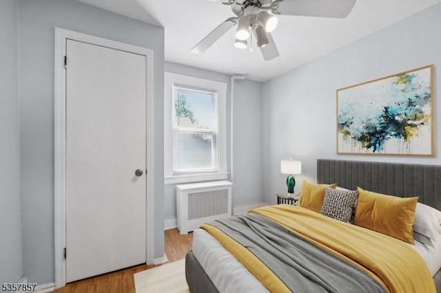 bedroom featuring radiator heating unit, wood finished floors, a ceiling fan, and baseboards
