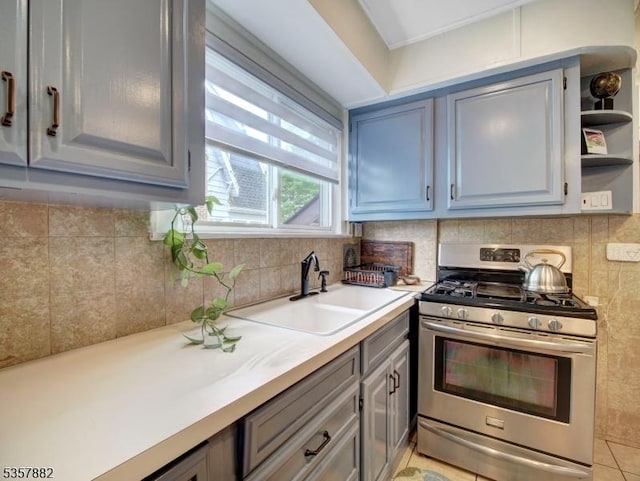 kitchen with stainless steel range with gas stovetop, a sink, gray cabinets, open shelves, and light countertops
