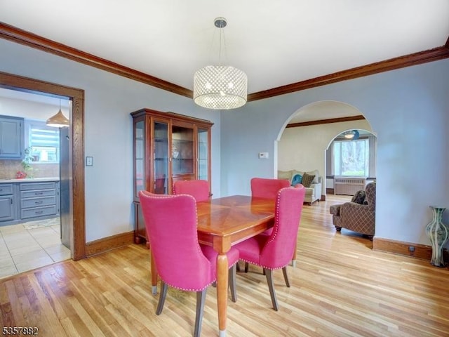 dining space featuring arched walkways, crown molding, light wood-type flooring, and baseboards