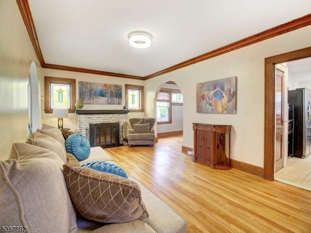 living room with arched walkways, light wood-style flooring, crown molding, baseboards, and a fireplace