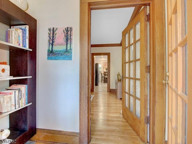 hallway featuring light wood-type flooring, baseboards, crown molding, and french doors