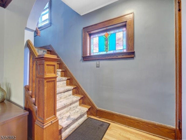 stairway featuring baseboards, wood finished floors, and arched walkways