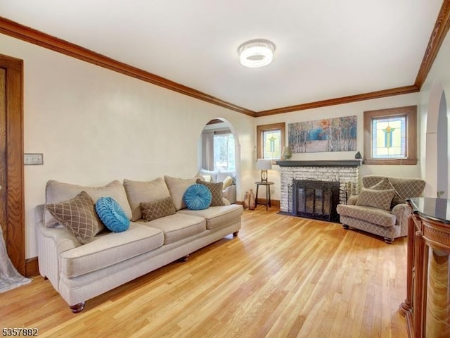 living area with arched walkways, light wood finished floors, crown molding, a brick fireplace, and baseboards