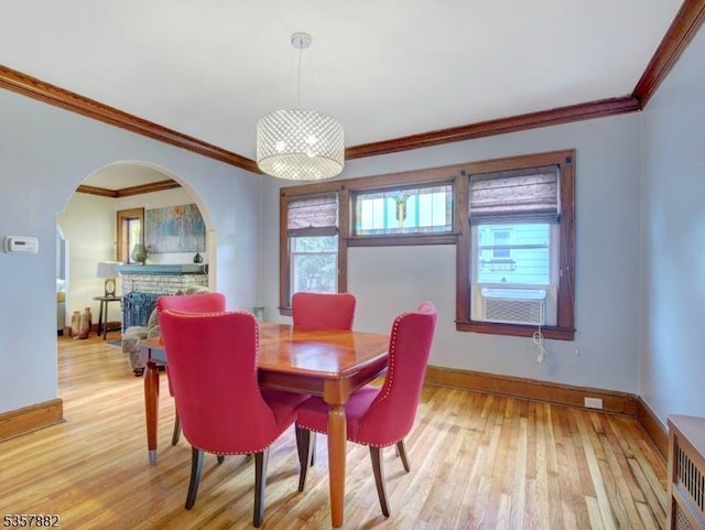dining room featuring arched walkways, ornamental molding, light wood-style flooring, baseboards, and a fireplace