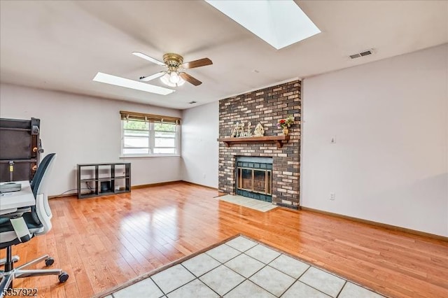 unfurnished office featuring a skylight, ceiling fan, light wood-style flooring, and a brick fireplace