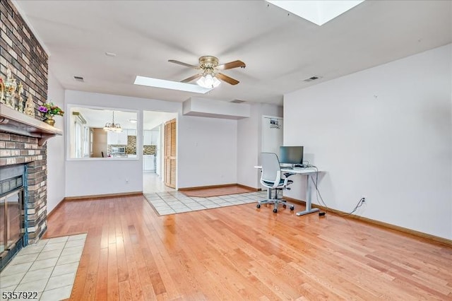 unfurnished office with a skylight, hardwood / wood-style flooring, a fireplace, a ceiling fan, and baseboards