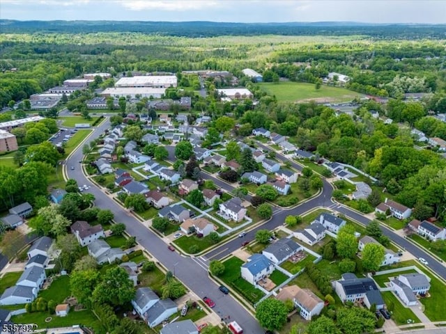 aerial view of property and surrounding area featuring a heavily wooded area and nearby suburban area