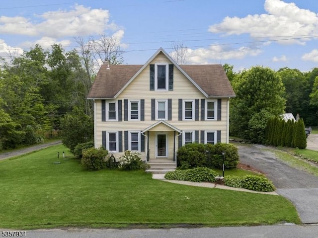 view of front of house featuring driveway, a chimney, and a front lawn