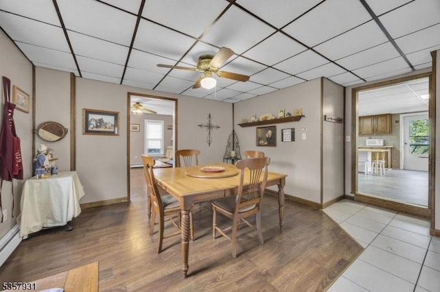 dining space featuring a drop ceiling, ceiling fan, wood finished floors, baseboards, and baseboard heating