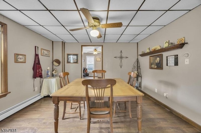 dining area with baseboard heating, a ceiling fan, wood finished floors, a paneled ceiling, and baseboards