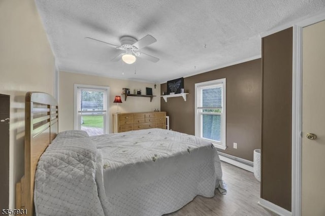bedroom featuring a baseboard heating unit, a textured ceiling, wood finished floors, baseboards, and a ceiling fan