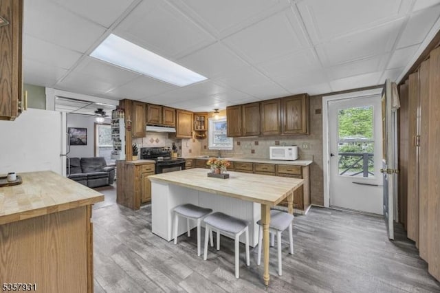 kitchen with wooden counters, white appliances, under cabinet range hood, light wood-style flooring, and brown cabinets