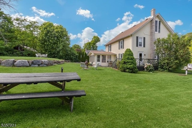rear view of house featuring a lawn, a chimney, and a deck