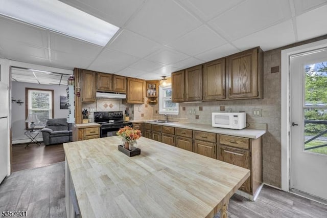 kitchen featuring white appliances, light wood-type flooring, under cabinet range hood, a sink, and brown cabinets