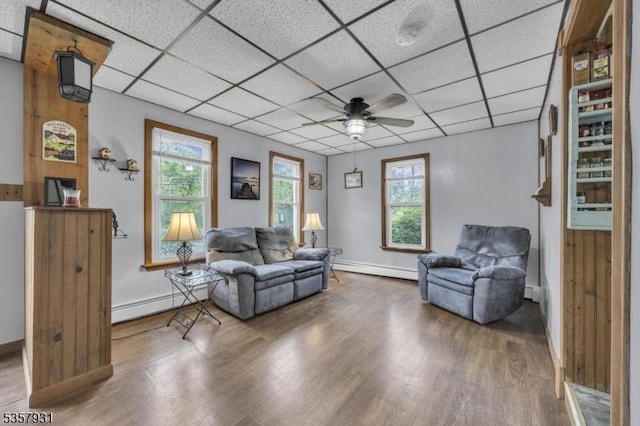 living room with baseboard heating, wood finished floors, a ceiling fan, baseboards, and a paneled ceiling