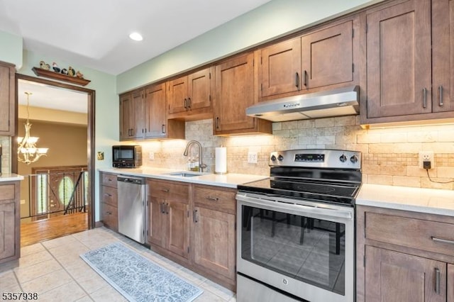 kitchen featuring stainless steel appliances, under cabinet range hood, a chandelier, a sink, and light countertops