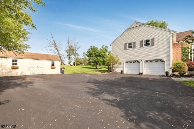 view of property exterior with driveway, an attached garage, an outdoor structure, a yard, and a barn