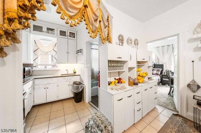 kitchen with stainless steel microwave, light tile patterned floors, a sink, white cabinetry, and light countertops