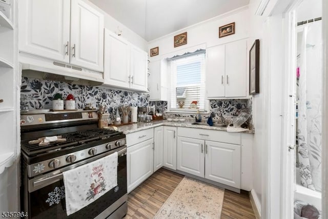 kitchen featuring stainless steel range with gas cooktop, under cabinet range hood, white cabinets, and backsplash