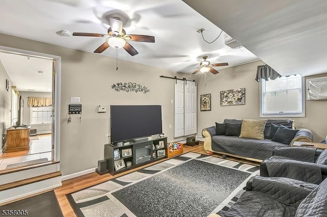 living room featuring a ceiling fan, a barn door, wood finished floors, and baseboards