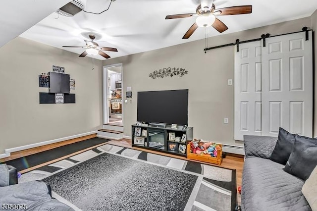 living area featuring ceiling fan, a barn door, wood finished floors, and baseboards