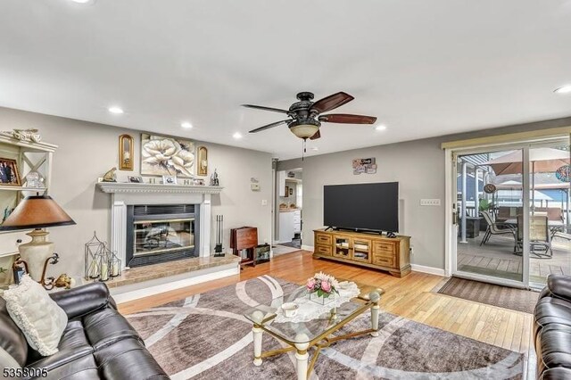 living area with a ceiling fan, wood finished floors, recessed lighting, a glass covered fireplace, and baseboards