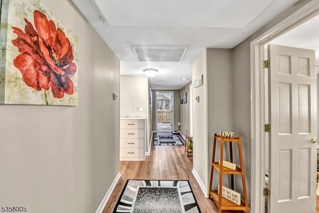 corridor with baseboards, light wood-style flooring, and attic access