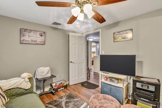 living area with wood finished floors, a ceiling fan, and baseboards