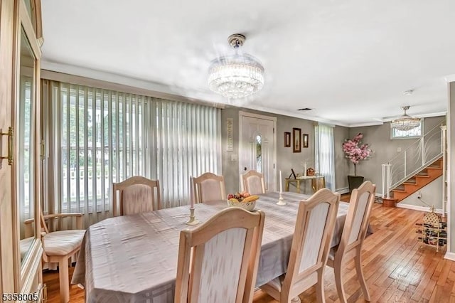 dining space featuring stairs, wood-type flooring, a chandelier, baseboards, and crown molding