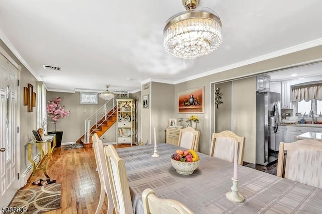dining space featuring stairway, light wood-type flooring, crown molding, a chandelier, and a baseboard heating unit