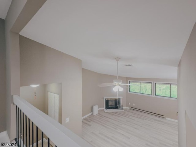 unfurnished living room with a baseboard heating unit, wood finished floors, a ceiling fan, a glass covered fireplace, and baseboards