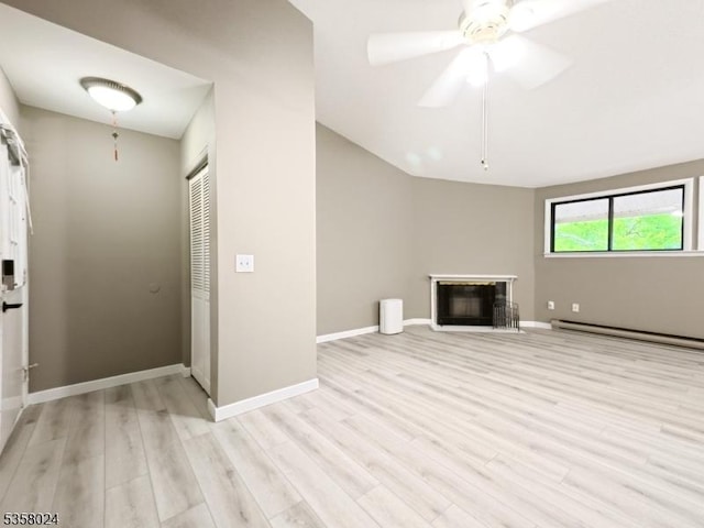 unfurnished living room featuring light wood-style flooring, a baseboard heating unit, a glass covered fireplace, baseboards, and a ceiling fan