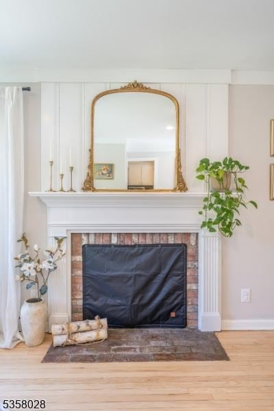 detailed view of a fireplace, wood finished floors, and baseboards