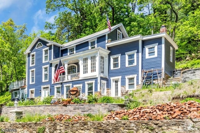 view of front of home with a balcony, a chimney, and view of scattered trees