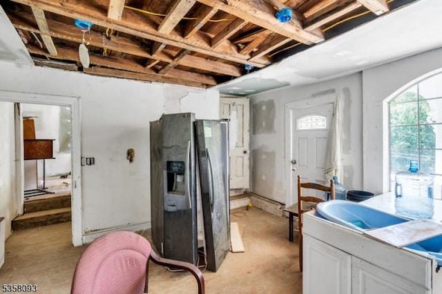 kitchen featuring fridge with ice dispenser, unfinished concrete floors, and white cabinetry