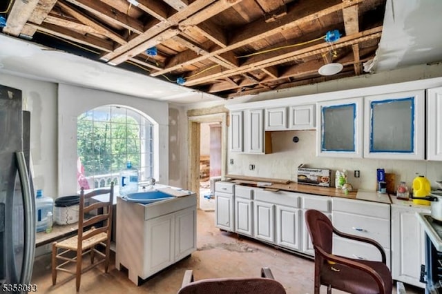 kitchen featuring refrigerator with ice dispenser, concrete floors, and white cabinets