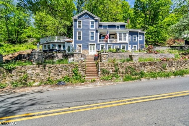 view of front facade with a balcony, stairway, and view of wooded area