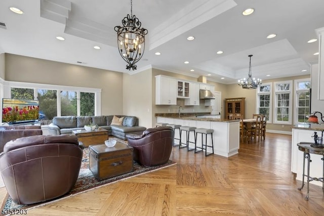living room with a chandelier, a raised ceiling, recessed lighting, and ornamental molding